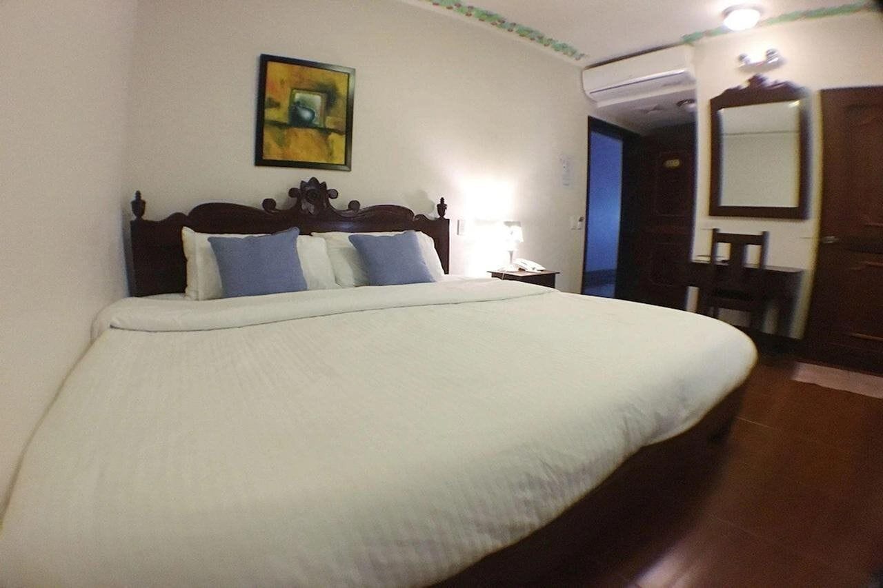 A bed with a wooden headboard, a bedside table with a lamp, and a painting on the wall.