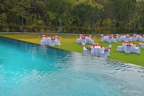 A poolside area with white tables and chairs, surrounded by greenery. - Urbane By Treat, Daman (Daman)