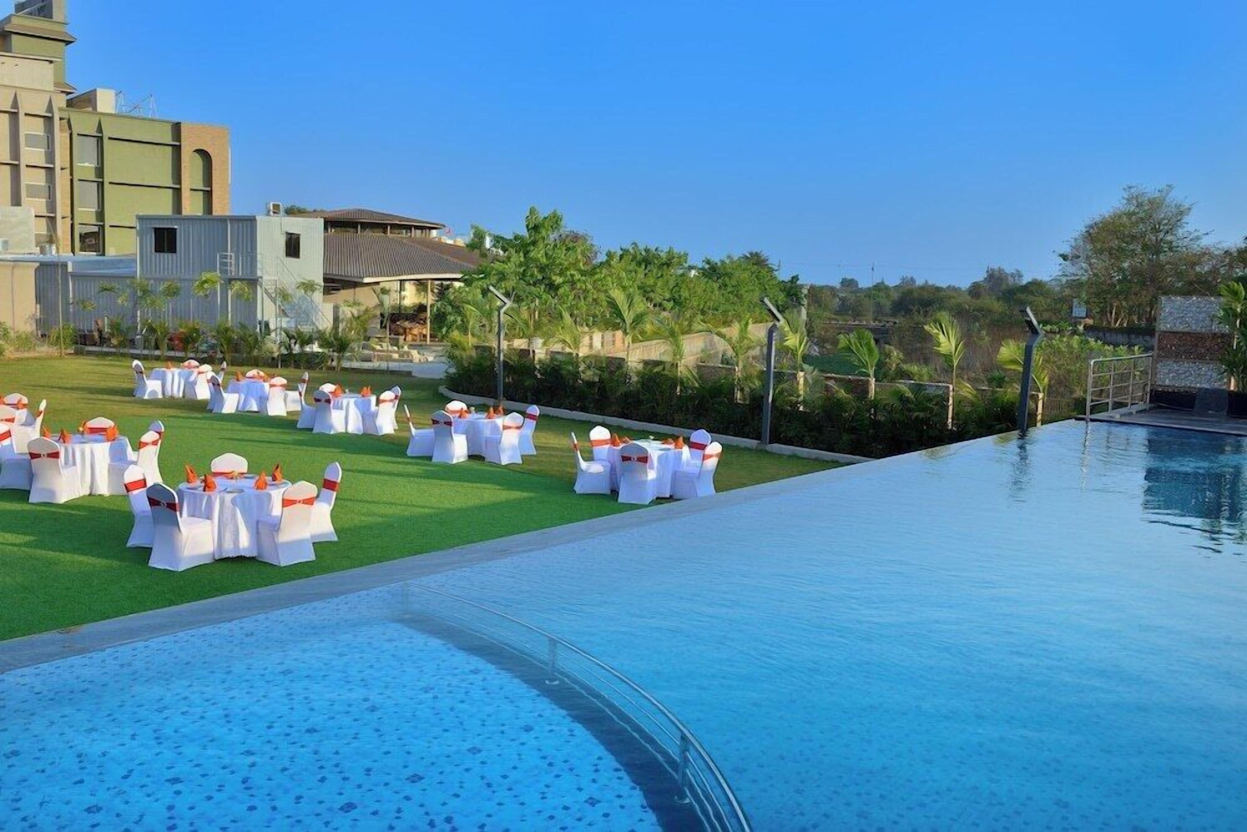 A poolside area with round tables and chairs, a clear sky, and buildings in the background.