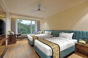 A hotel room with two beds, a desk, and a view of greenery outside. - Urbane By Treat, Daman (Daman)