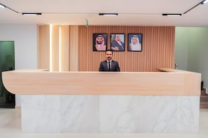 A reception desk with a marble top and a wooden backdrop with framed portraits. - Tura Residence Sulemania (Riyadh)