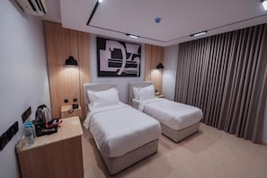 A hotel room with two beds, a wooden panel wall, a large abstract artwork, and a curtain on the window. - Tura Residence Sulemania (Riyadh)
