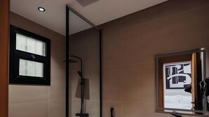 A modern bathroom with a glass shower enclosure, a toilet, a sink with a mirror, and a trash bin. - Tura Residence Sulemania (Riyadh)