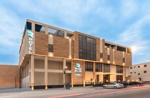 A modern hotel with a prominent 'HOTEL' sign, a large entrance with a covered area, and a parking lot with cars. - Rhenium Hotel (Riyadh)
