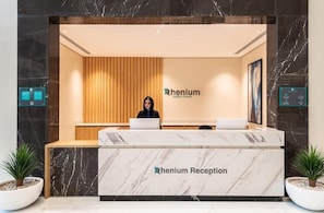Un mostrador de recepción con encimera de mármol que dice “Rhenium Reception”, un panel de pared de madera y dos plantas en macetas.