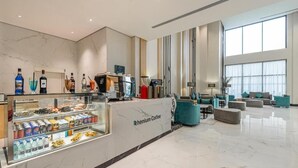 Eine moderne Hotelhalle mit einer Kaffeestation, Sitzgelegenheiten und großen Fenstern.