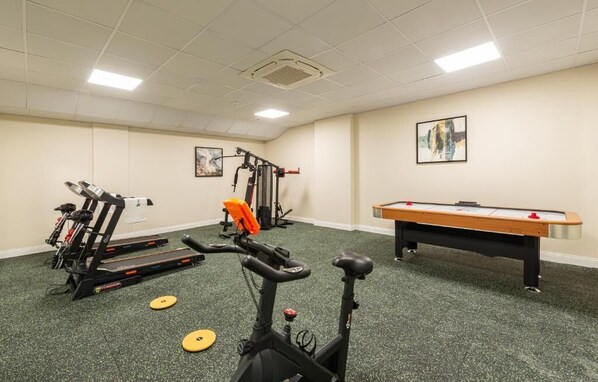 A gym with exercise equipment, a pool table, and artwork on the walls.