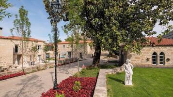 A courtyard with stone buildings, a statue, and red flowers.
