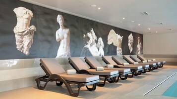 Una hilera de tumbonas con un gran mural en la pared que muestra esculturas clásicas.