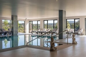 A modern indoor swimming pool with clear glass walls, lounge chairs, and a Buddha statue. - Vila Gale Collection Ponte de Lima Vineyards (Ponte de Lima)