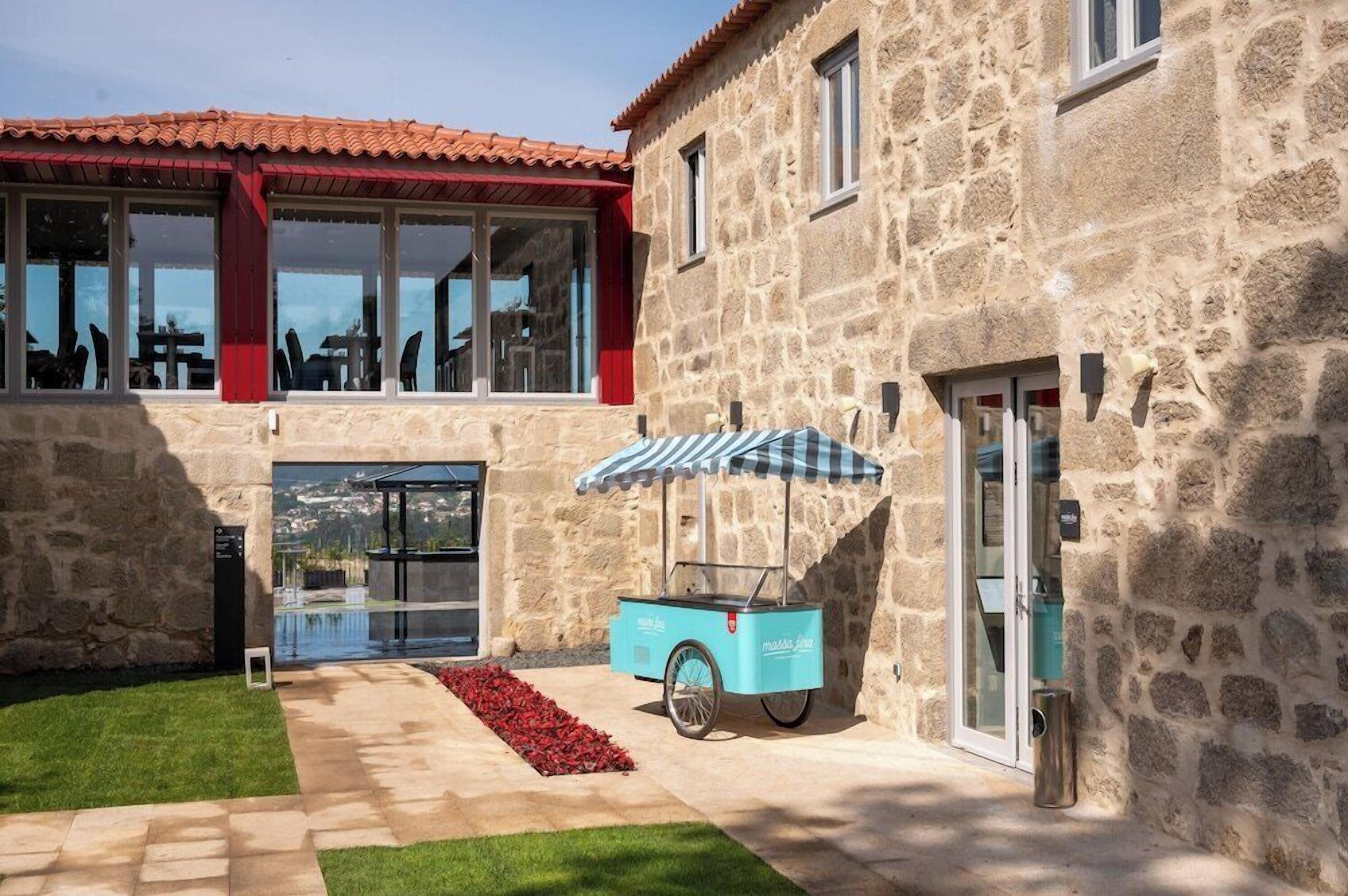Un edificio de piedra con techo de tejas rojas, un área de estar al aire libre cubierta y un carrito de comida.