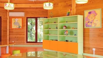 A room with wooden walls, a glass table, orange and green shelves with toys, and a large window.