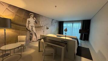 A hotel room with a bed, a desk, a chair, a lamp, and a large wall mural.