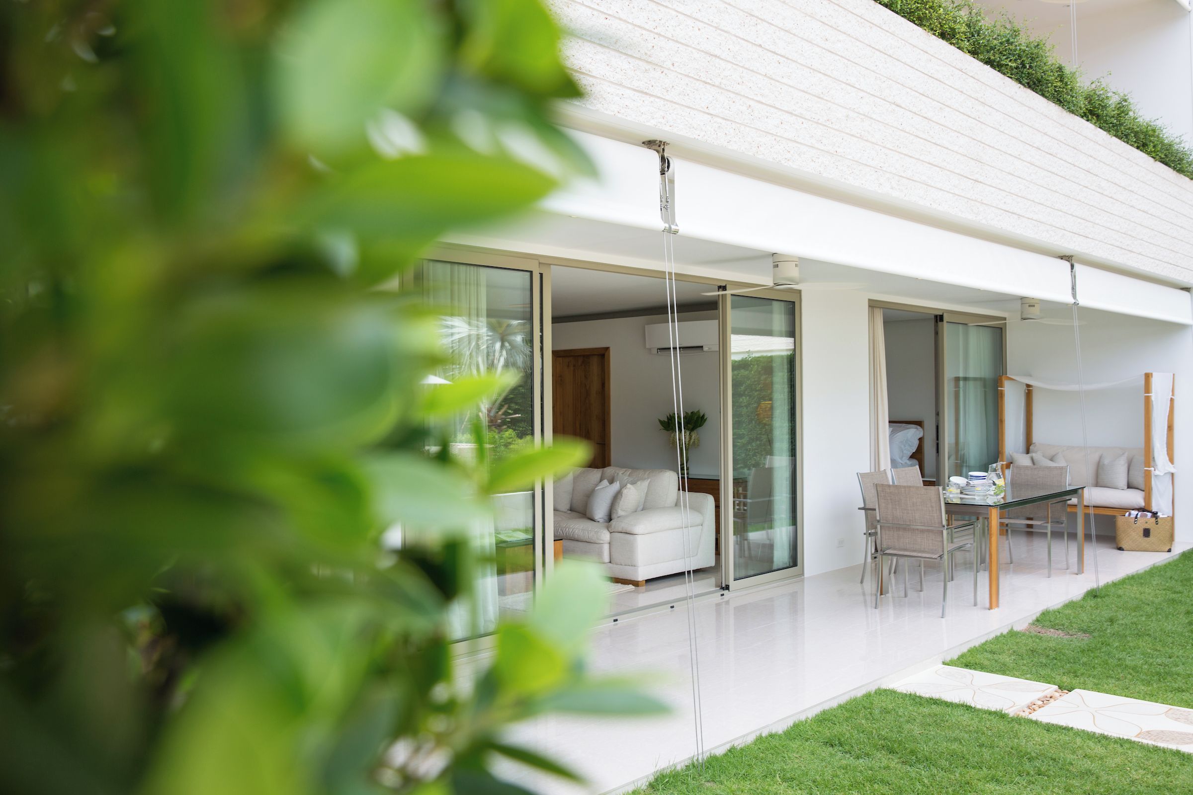 A modern house with a glass door leading to a living area, a dining table with chairs, and a small garden.