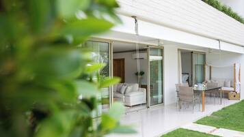 A modern house with a glass door leading to a living area, a dining table with chairs, and a small garden.