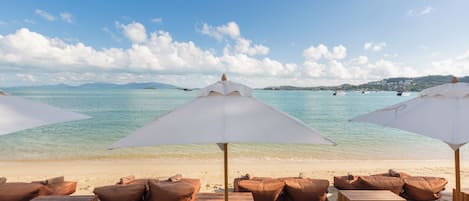 A beach with sun loungers and umbrellas, a clear sky, and calm waters.