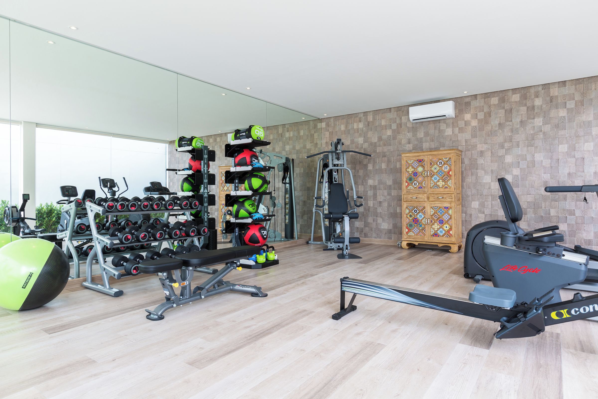A modern gym with various exercise equipment, including dumbbells, a bench, and cardio machines.