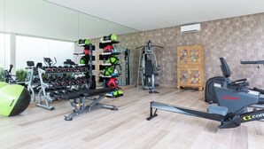 A modern gym with various exercise equipment, including dumbbells, a bench, and cardio machines.