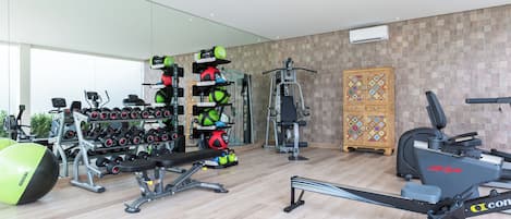 A modern gym with various exercise equipment, including dumbbells, a bench, and cardio machines.