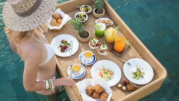 A person with a tray containing food and drinks by a pool.