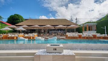 A pool area with lounge chairs and umbrellas, a bar area with seating, and a building with a tiled roof.