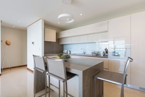 A modern kitchen with a central island, bar stools, a built-in oven, and a large window. - Chi The Residence (Koh Samui)