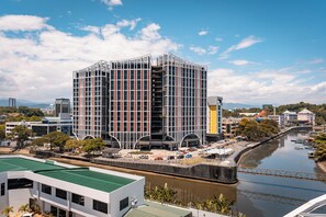 Un edificio moderno con fachada de entramado, ubicado junto a un río y un puente al fondo.