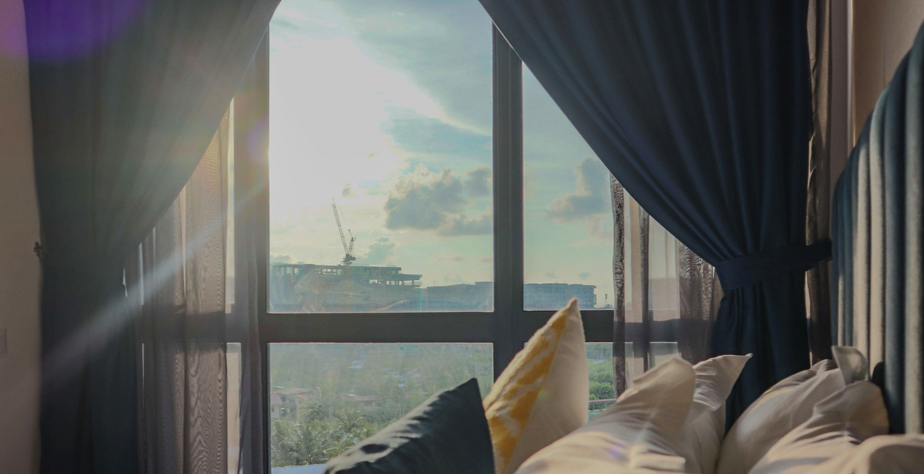 A room with a large window, a bed with pillows, and a view of a ship outside.