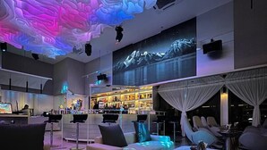 A modern lounge area with a bar, seating, and a large screen displaying a mountain landscape. - The Sigar Hotel (Kota Kinabalu)