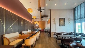 A restaurant interior with wooden tables and chairs, a central seating area with a sofa, and pendant lighting. - The Sigar Hotel (Kota Kinabalu)