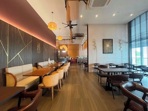 A restaurant interior with wooden tables and chairs, a central seating area with a sofa, and pendant lighting. - The Sigar Hotel (Kota Kinabalu)