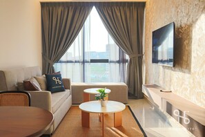 Una habitación de hotel moderna con sofá, una pequeña mesa redonda, televisor de pantalla plana en la pared y un amplio ventanal con cortinas.