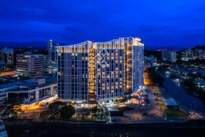 Un hotel moderno con una fachada geométrica distintiva, rodeado de otros edificios y un estacionamiento.