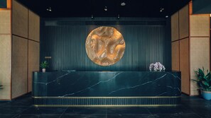Una recepció amb taulell de marbre, una obra d'art circular a la paret i plantes en testos.