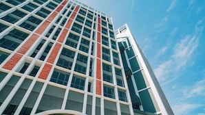 A modern high-rise building with a distinctive red and white facade, large windows, and a clear sky in the background. - The Sigar Hotel (Kota Kinabalu)