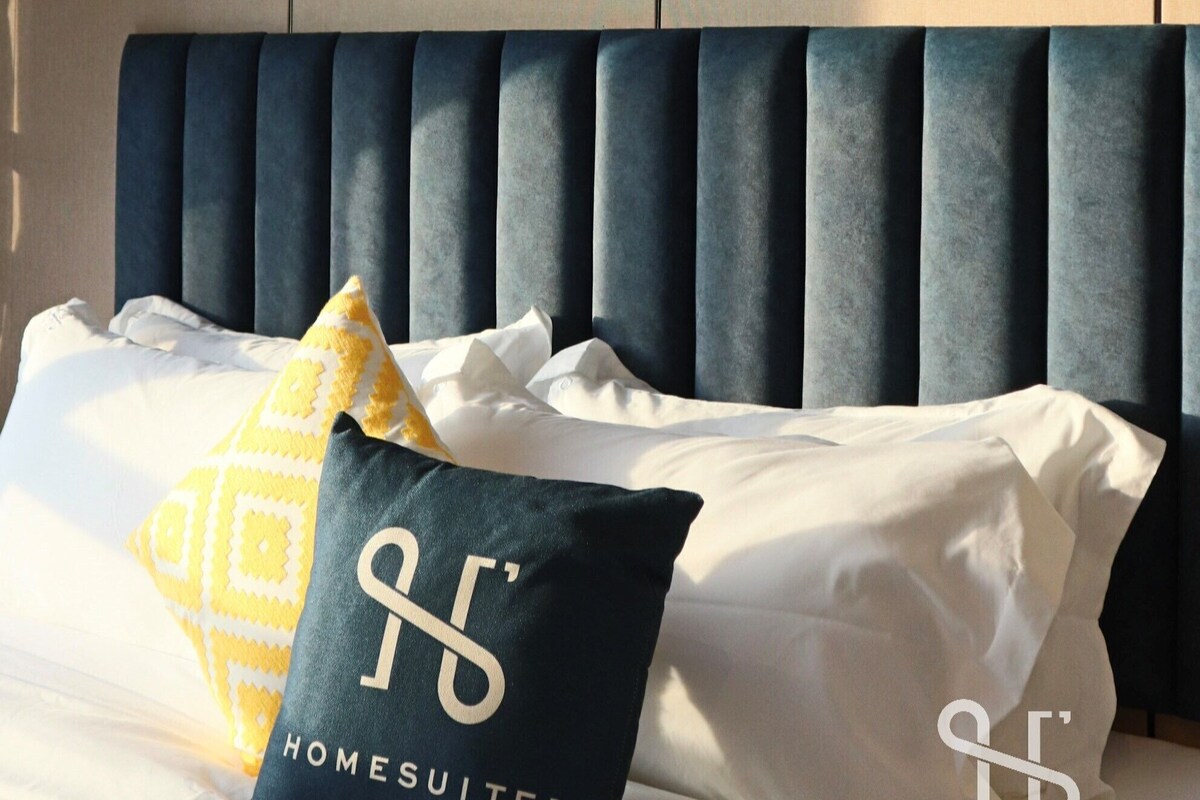A hotel room with a bed, a framed picture of a mountain landscape, and a headboard.