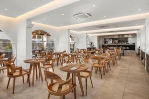 Un comedor amplio con varias mesas y sillas, una cocina al fondo y un diseño interior moderno.
