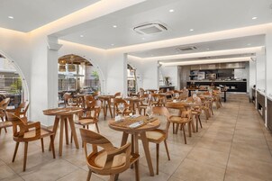 Un comedor amplio con varias mesas y sillas, una cocina al fondo y un diseño interior moderno.