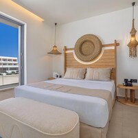 Habitación de hotel con una cama grande, una mesita de noche, una lámpara de pared y vistas al exterior.