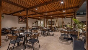 An outdoor dining area with multiple tables and chairs, wooden ceiling beams, and potted plants. - Cabana White Boutique Hotel & Suites (Kos)