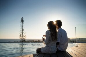 Una pareja sentada junto a la piscina, con vista despejada al océano y un árbol distante.