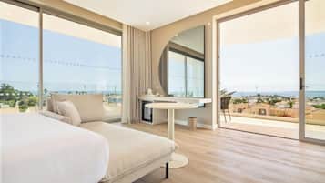 A modern hotel room with a large bed, a round table, and a view of the sea.