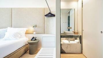 Een moderne hotelkamer met een bed, nachtkastje, lamp en uitzicht op de badkamer.