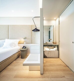 A modern hotel room with a bed, bedside table, lamp, and a view of the bathroom. - Ananea Castelo Suites Algarve (Albufeira)