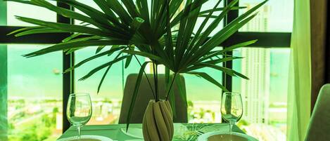 A dining table with two plates and a vase with a plant, set against a window with a view of buildings.