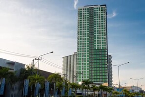 Een hoog, modern gebouw met een ruitpatroon, omgeven door palmbomen en lantaarns.