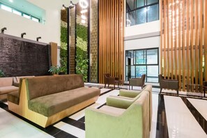 Een moderne lobby met een bank, stoelen, een decoratieve wand en een groot raam.