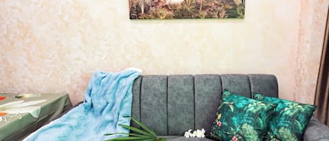 A room with a grey sofa, a blue blanket, a tropical-themed pillow, and a plant.