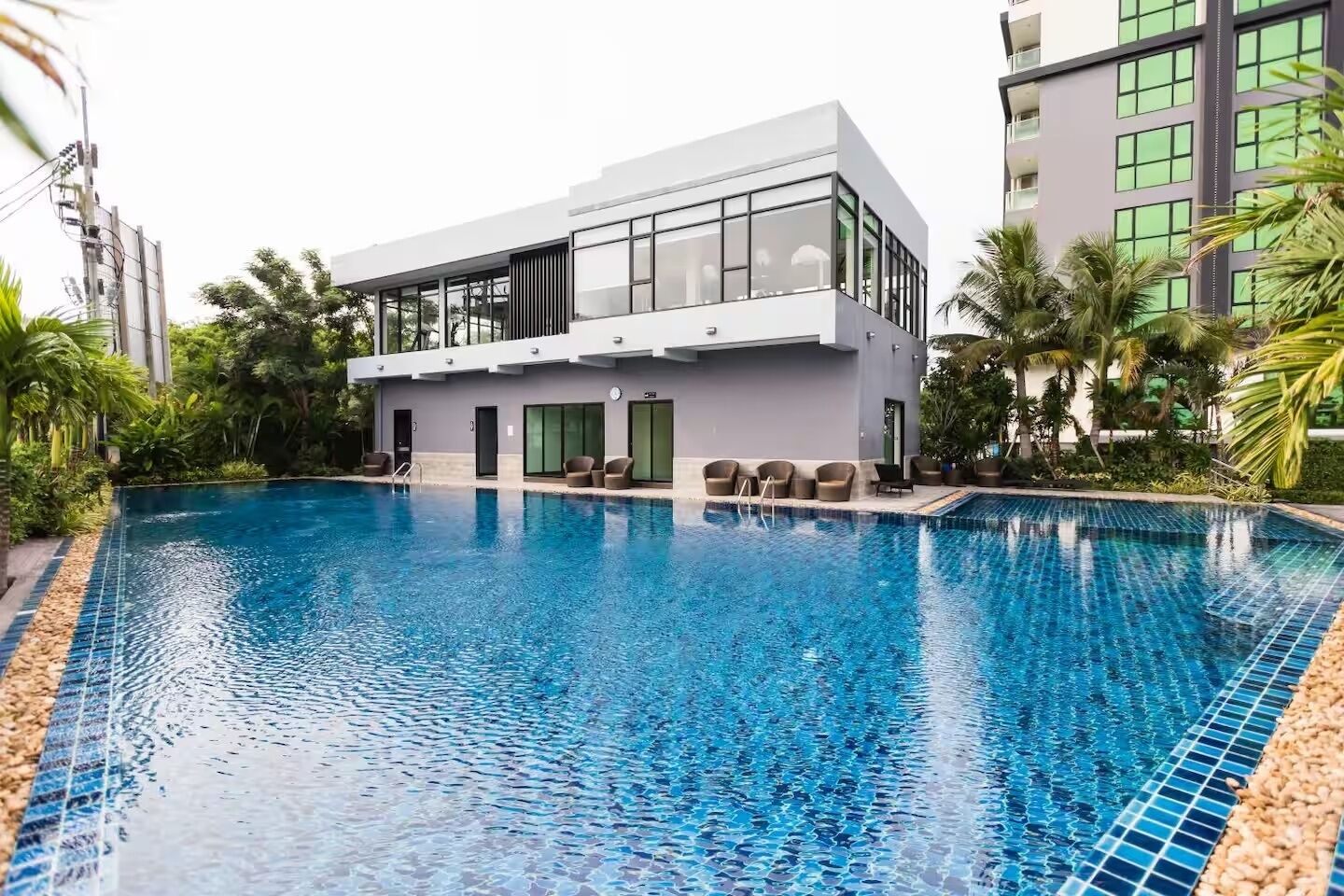 A modern hotel with a swimming pool, outdoor seating, and lush greenery.