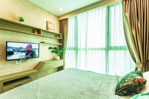 Ein Hotelzimmer mit Fernseher an der Wand, einem Bett mit gemustertem Überwurf, einer Topfpflanze und einem Fenster mit Vorhängen.